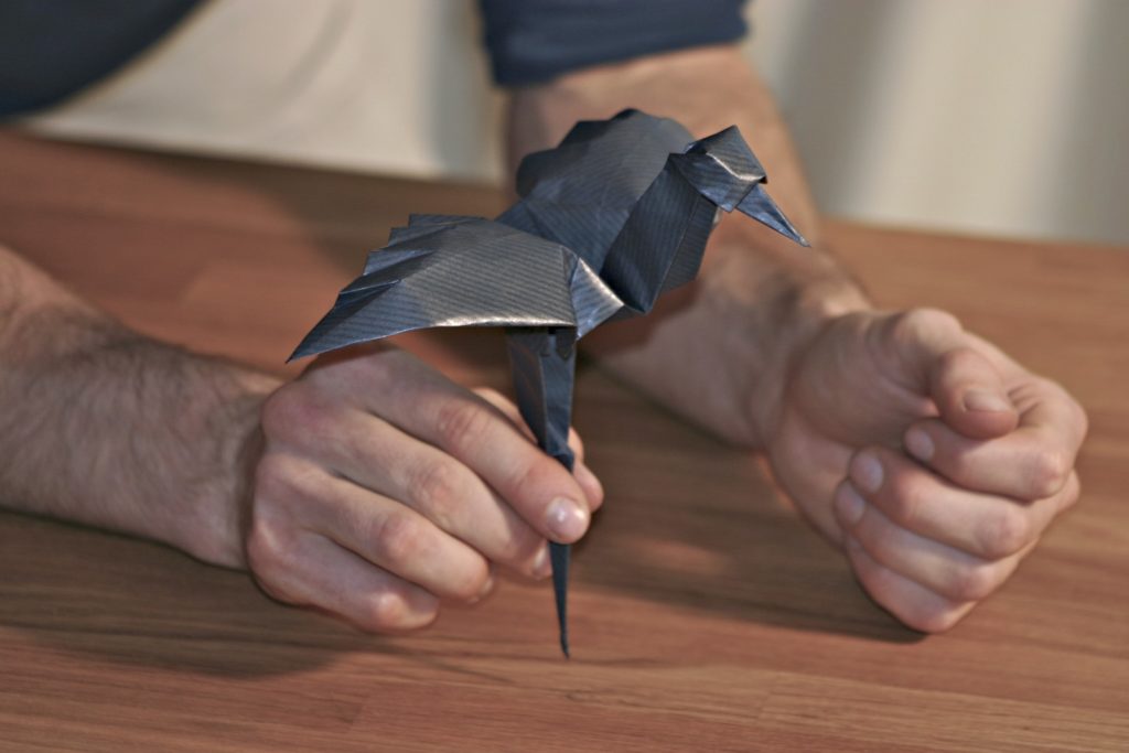 Mains de l'artiste pliant un oiseau en papier noir