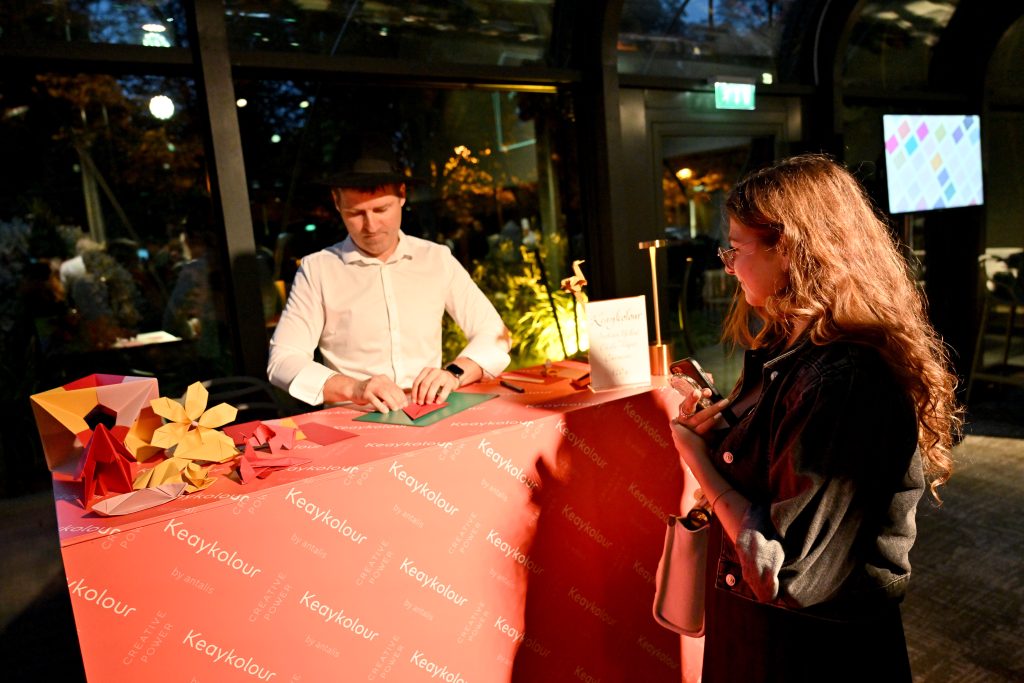 Kevin Briez plie un origami pour une invitée sur un stand lors d'un événement