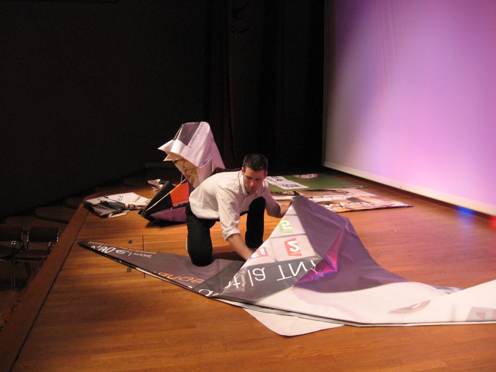 Kevin Briez pliant une feuille géante sur scène lors d'une performance démonstrative en origami